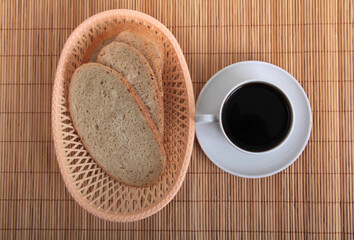 Cup of coffee and bread on a wicker bamboo mat