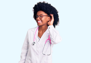 Young african american woman wearing doctor coat and stethoscope smiling with hand over ear listening an hearing to rumor or gossip. deafness concept.