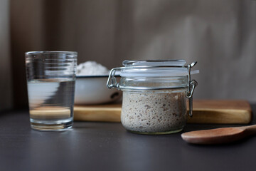 Active rye sourdough starter in a jar, a glass of water and a bowl with flour.