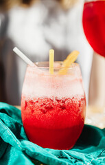 red fruit cocktail in a glass with a straw on a blue napkin