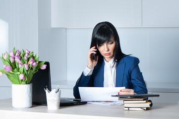 Businesswoman brunette in a suit at her desk talking on his mobile phone . Office work concept