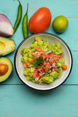 Mexican guacamole with chili pepper and tomato on turquoise background