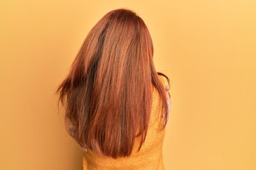 Beautiful redhead woman wearing casual winter sweater over yellow background hugging oneself happy...