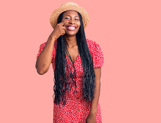 Young african american woman wearing summer hat pointing with hand finger to face and nose, smiling cheerful. beauty concept