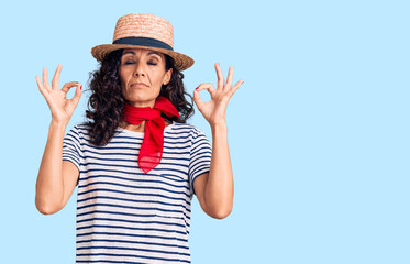 Obraz na płótnie Canvas Middle age beautiful woman wearing casual striped t shirt and summer hat relax and smiling with eyes closed doing meditation gesture with fingers. yoga concept.