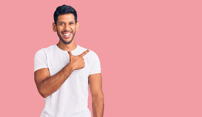 Young latin man wearing casual clothes cheerful with a smile on face pointing with hand and finger up to the side with happy and natural expression