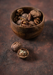 Walnuts kernels and whole on a dark desk. Whole walnut in wood vintage bowl in background. Selective focus.