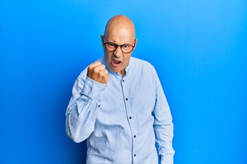 Middle age bald man wearing casual clothes and glasses angry and mad raising fist frustrated and furious while shouting with anger. rage and aggressive concept.