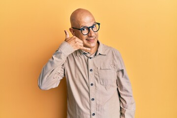 Middle age bald man wearing casual clothes and glasses smiling doing phone gesture with hand and fingers like talking on the telephone. communicating concepts.