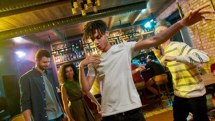 Cheerful mixed race young man dancing at party in the bar. Friends celebrating, having fun in the background