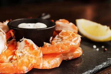 shrimp around a metal sauce pan with a slice of lemon on a black mica Board
