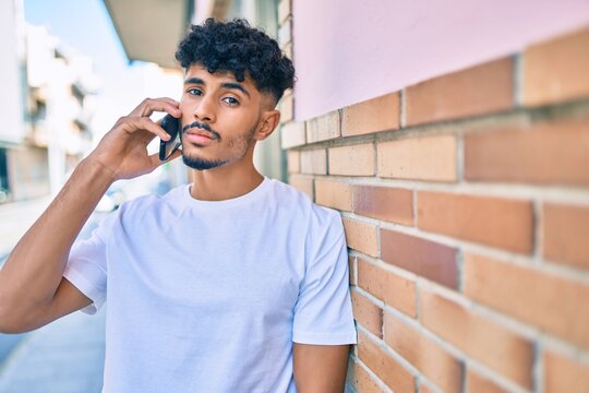 Young arab man with serious expression talking on the smartphone leaning on the wall.