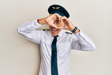 Handsome middle age mature man wearing airplane pilot uniform doing heart shape with hand and fingers smiling looking through sign