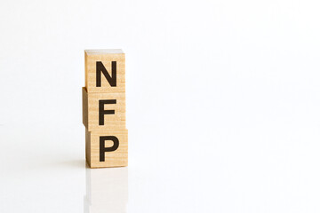 Three wooden cubes with letters NFP - Nonfarm payrolls, on white table, more in background, space for text in right down corner