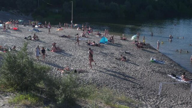 A crowd of people on the beach sunbathing and relaxing. People swim in the lake on a hot summer day. Weekends, vacations. The lifting of the quarantine