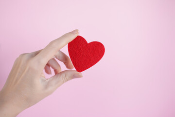 female hand holding a red heart on pink backround. The concept of sincere devotion to faith. Donation, life saving or charity concept. Close-up