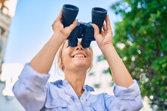 Young blonde woman smiling happy looking for new opportunity using binoculars at the park,