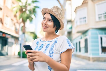 Fototapeta premium Young latin tourist girl on vacation smiling happy using smartphone at the city.