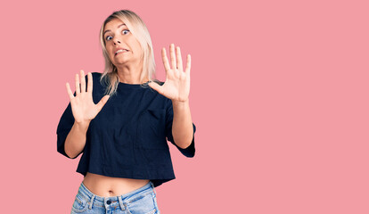 Young beautiful blonde woman wearing casual t-shirt afraid and terrified with fear expression stop gesture with hands, shouting in shock. panic concept.