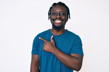 Young african american man with braids wearing casual clothes cheerful with a smile of face pointing with hand and finger up to the side with happy and natural expression on face