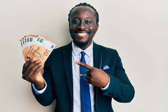 Handsome young black man wearing business suit holding 50 euros banknotes smiling happy pointing with hand and finger