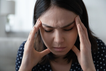Close up of unhealthy young asian woman struggle with migraine or headache at home. Unwell millennial Vietnamese female have dizziness or blurry vision. Girl suffer from mental psychological problems.