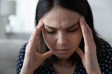 Close up of unhealthy young asian woman struggle with migraine or headache at home. Unwell...