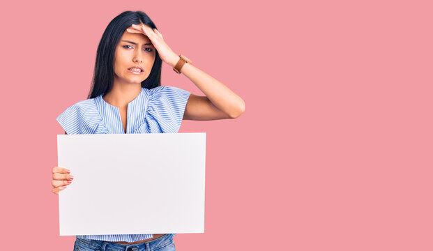 Young beautiful latin girl holding blank empty banner stressed and frustrated with hand on head, surprised and angry face
