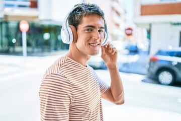 Young handsome caucasian man smiling happy listening to music using headphones walking at city.