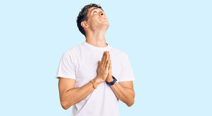 Young handsome man wearing casual white tshirt begging and praying with hands together with hope...