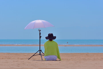 Woman sitting under reflection photo umbrella on the beach with her back to the viewer