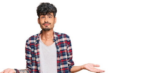 Young hispanic man wearing casual clothes clueless and confused expression with arms and hands...