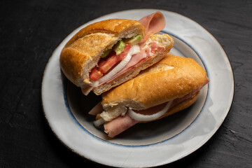 Mexican ham sandwich with avocado and cheese also called torta on dark background