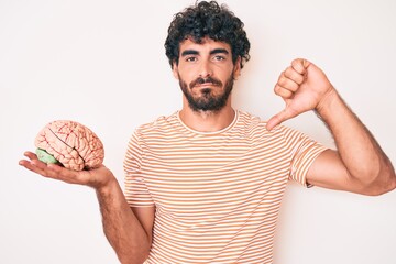Handsome young man with curly hair and bear holding brain as mental health concept with angry face,...