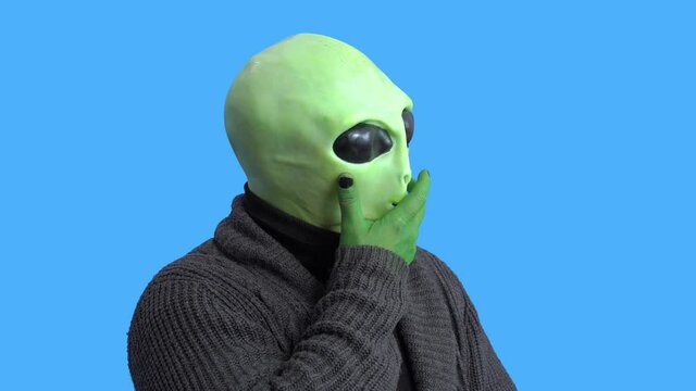 Blogger in funny alien costume and home outfit sits in front of camera to record video to create interesting entertainment content for vlog. Themed costume for party. Gesture of fright or surprise.
