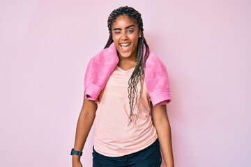 Young african american woman with braids wearing sportswear and towel winking looking at the camera...