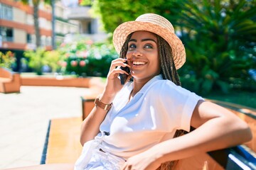 Young african american woman with braids smiling happy using smartphone outdoors on a sunny day of summer