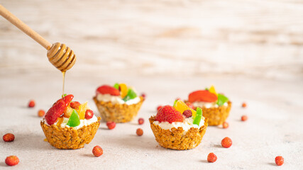 Honey dripping from dipper on healthy homemade cupcakes with strawberries. banana and dried fruits on bright background