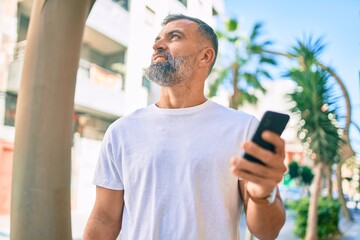 Middle age grey-haired man smiling happy using smartphone at the city