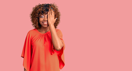 Obraz na płótnie Canvas Young african american woman wearing casual clothes covering one eye with hand, confident smile on face and surprise emotion.
