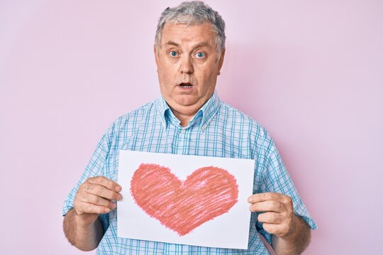 Senior grey-haired man holding heart draw clueless and confused expression. doubt concept.