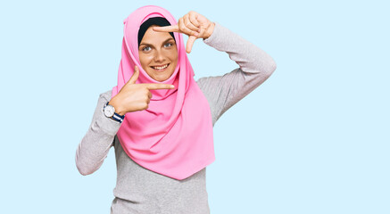 Obraz na płótnie Canvas Young caucasian woman wearing traditional islamic hijab scarf smiling making frame with hands and fingers with happy face. creativity and photography concept.