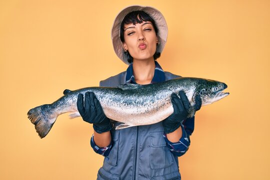 Beautiful brunettte fisher woman showing raw salmon looking at the camera blowing a kiss being lovely and sexy. love expression.