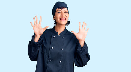 Young brunette woman with short hair wearing professional cook uniform showing and pointing up with fingers number ten while smiling confident and happy.