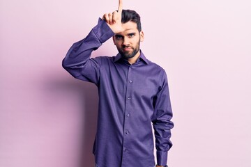 Fototapeta premium Young handsome man with beard wearing casual shirt making fun of people with fingers on forehead doing loser gesture mocking and insulting.