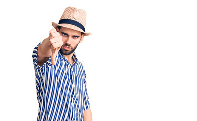 Young handsome man with beard wearing summer hat and striped shirt looking unhappy and angry showing rejection and negative with thumbs down gesture. bad expression.