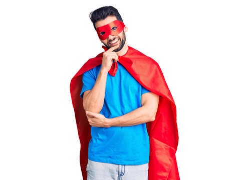 Young handsome man with beard wearing super hero costume looking confident at the camera with smile with crossed arms and hand raised on chin. thinking positive.