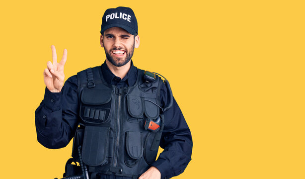 Young handsome man with beard wearing police uniform smiling with happy face winking at the camera doing victory sign. number two.