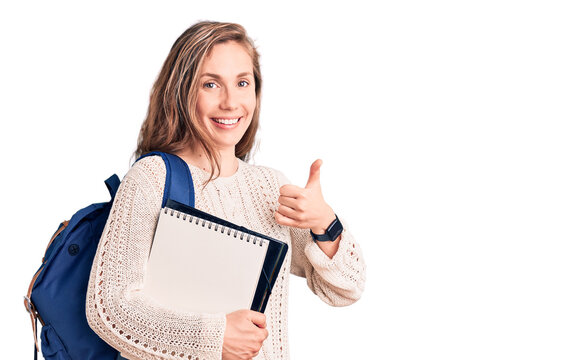 Young beautiful blonde woman wearing student backpack holding notebook smiling happy and positive, thumb up doing excellent and approval sign