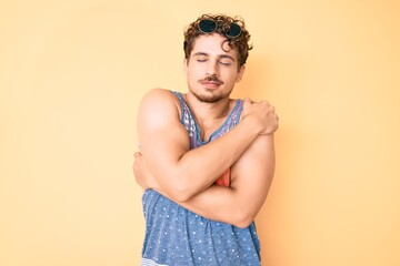 Young caucasian man with curly hair wearing casual style with sleeveless shirt hugging oneself...